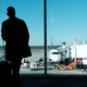 Person stands at airport gate looking out window at plane